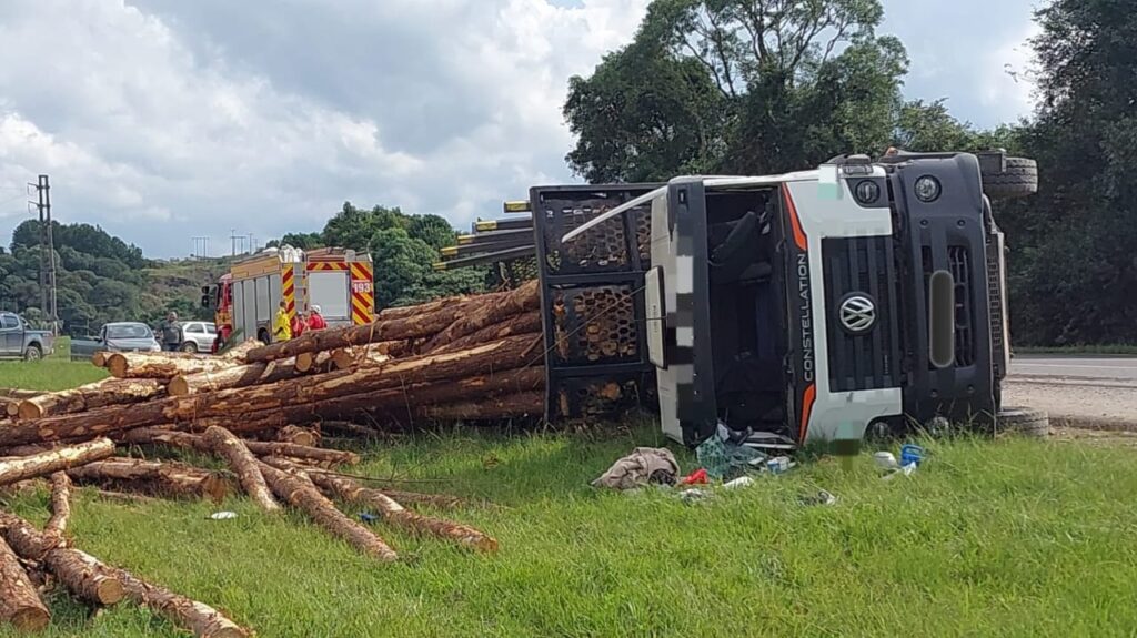 Caminhão carreta carregado com toras de madeiras tomba após colisão